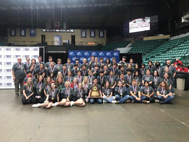 60 students and staff members in an event center with a championship trophy and gold medals 